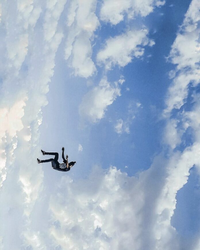 A thrilling aerial view of skydiver freefalling against a dramatic cloud-filled blue sky.